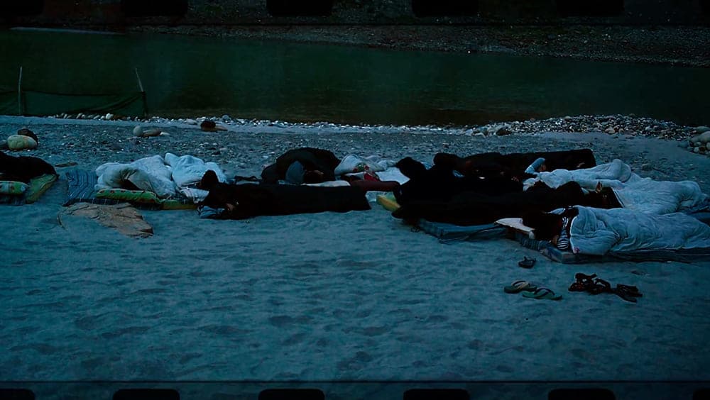 People lying down at the river bank under open skies.