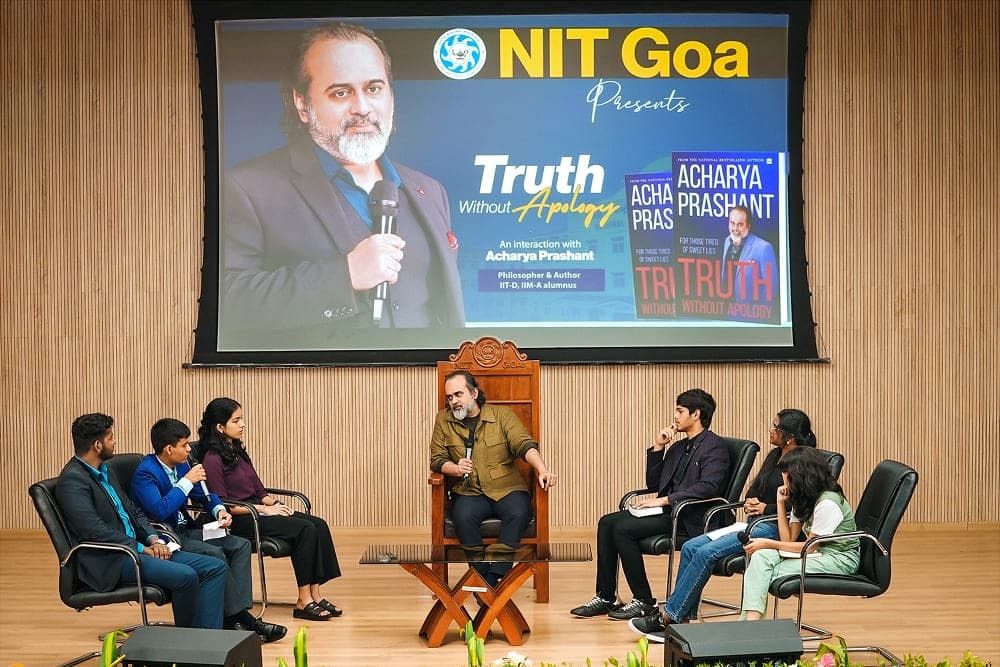 Acharya Prashant sitting on stage with students answering questions