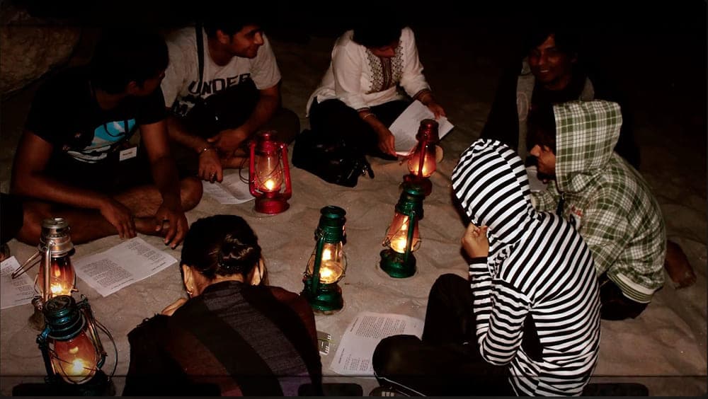 People sitting around at night under lantern lights reading.