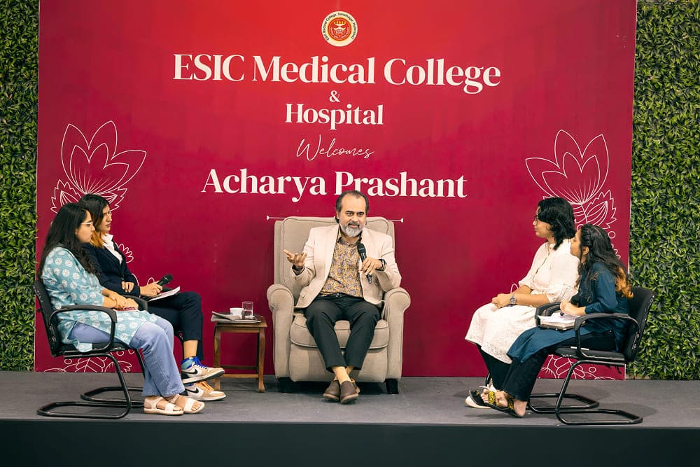 Acharya Prashant sitting on stage with students answering questions