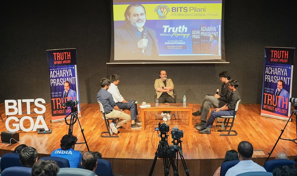 Acharya Prashant sitting on stage with students answering questions